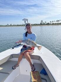 Young angler proudly holding a large fish while sitting on the bow of a boat in calm waters.