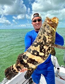 Angler proudly displaying a large Goliath Grouper while fishing in coastal waters.