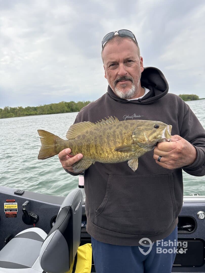 Angler proudly displaying a large Smallmouth Bass while fishing from a boat, showcasing a successful day on the water.
