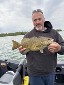 Angler proudly displaying a large Smallmouth Bass while fishing from a boat, showcasing a successful day on the water.