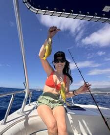 Angler proudly displaying a catch of yellow fish while aboard a boat in clear blue waters.