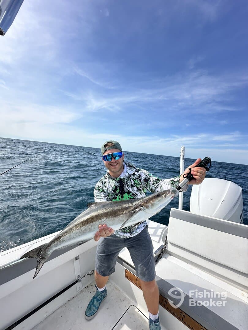 Angler proudly displaying a large fish while fishing on a boat in open water.