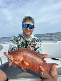 Angler proudly displaying a vibrant Red Snapper while fishing offshore, showcasing a successful day on the water.