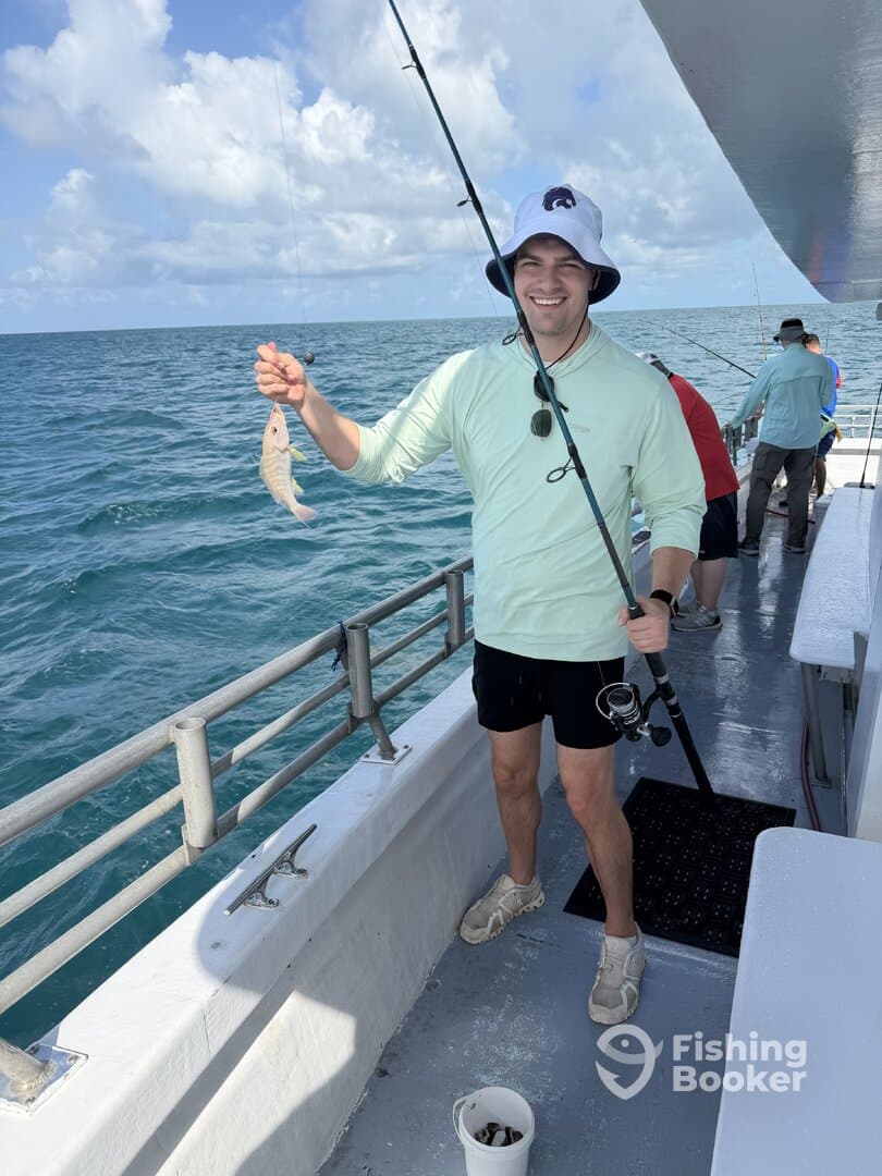 A happy angler holding a small fish while fishing on a boat in clear blue waters, showcasing a fun day of fishing.