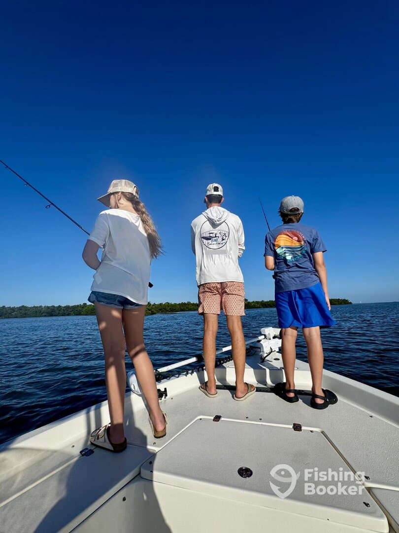 Three young anglers casting lines from the bow of a boat in a serene fishing environment, enjoying a sunny day on the water.