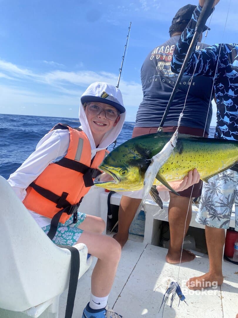 A young angler proudly holding a vibrant Mahi Mahi while fishing offshore, showcasing a fun family fishing experience.