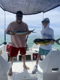 A proud moment on the water as a father and son duo display their catches, a Mahi Mahi and a smaller fish, while enjoying a sunny day on a fishing charter.