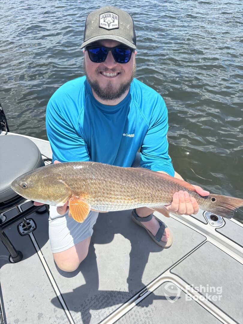 Angler proudly displaying a large Redfish while fishing on a sunny day.