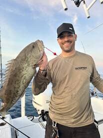 Angler proudly displaying a large Grouper while fishing on a boat in open waters.