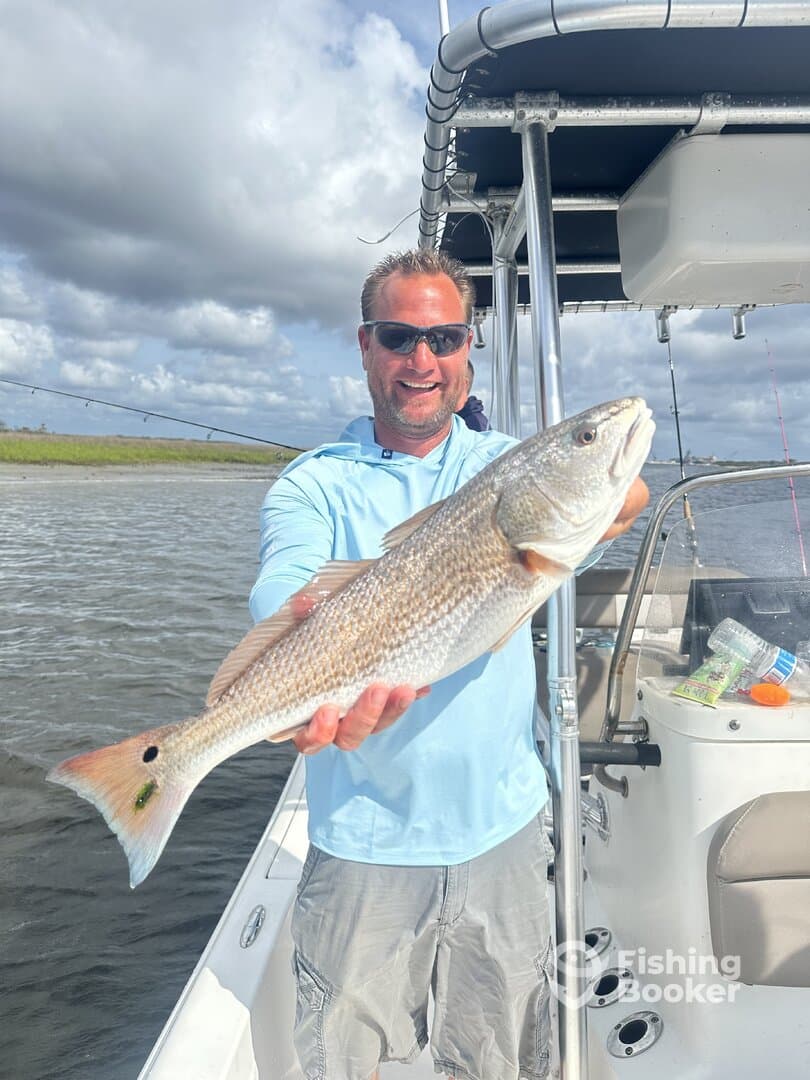 Angler proudly displaying a Redfish while fishing from a boat in a coastal waterway.