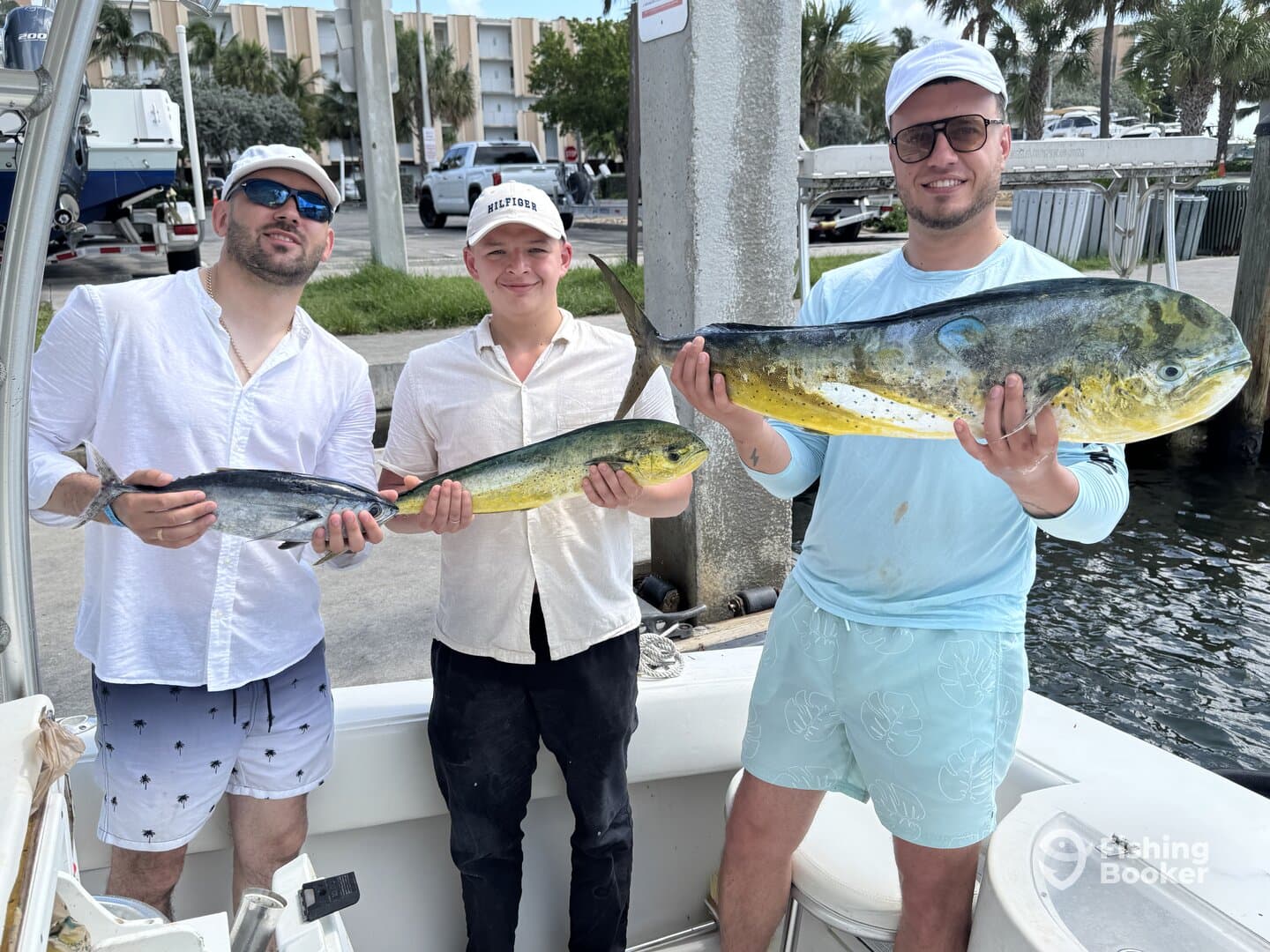 Three anglers proudly displaying their catch of Mahi Mahi and a smaller fish at the dock, showcasing a successful day of fishing.