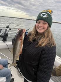 A happy angler proudly displaying a freshly caught Lake Trout while fishing on a boat, showcasing a beautiful day on the water.
