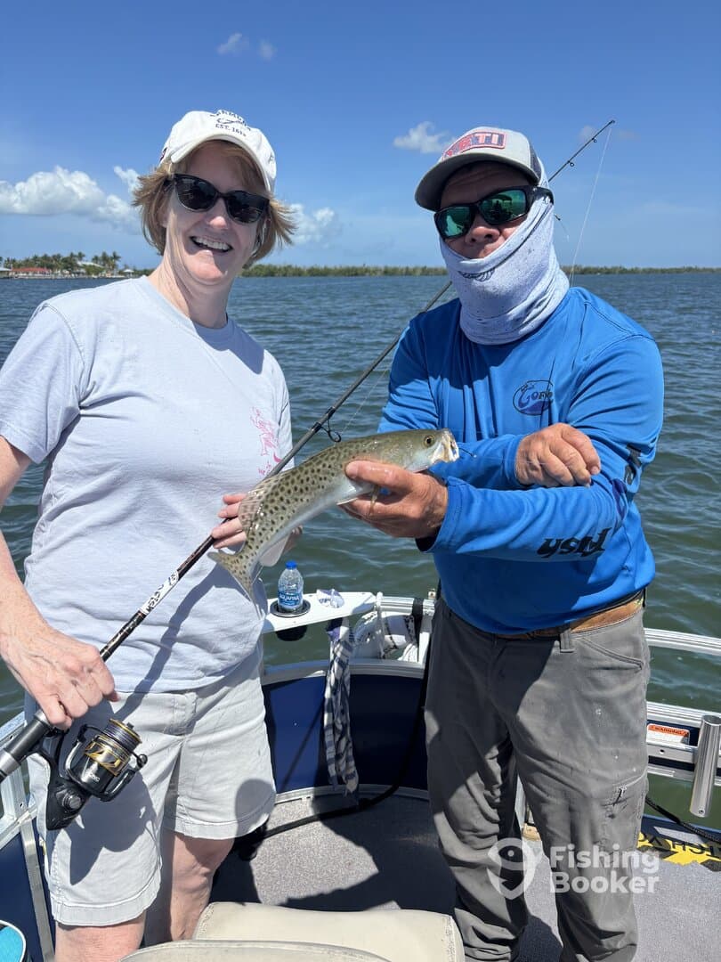 A woman and a guide proudly display a Speckled Trout while fishing on a boat, enjoying a sunny day on the water.