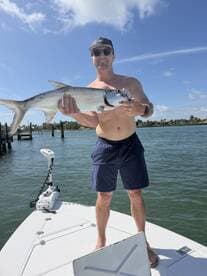 Angler proudly displaying a large Tarpon while standing on the bow of a boat in a sunny fishing environment.