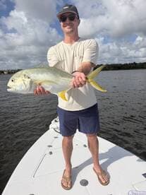 Angler proudly displaying a large Jack Crevalle while standing on the bow of a boat in a scenic fishing environment.