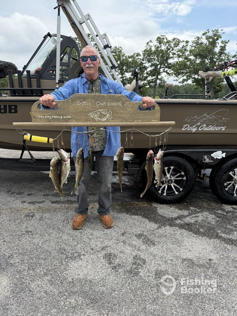An angler proudly displaying a catch of several fish on a wooden board, showcasing a successful fishing trip with Doty Outdoors.