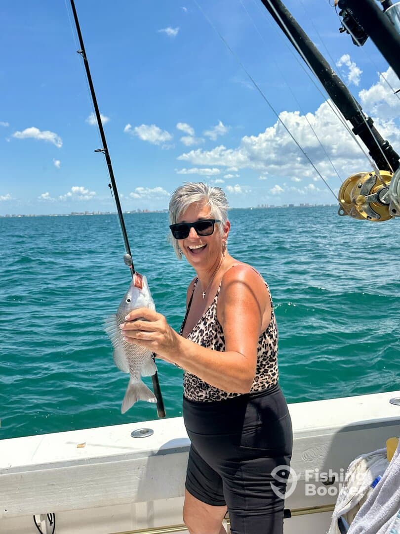 A smiling angler proudly displaying a Snapper while fishing on a sunny day, showcasing the excitement of a successful catch.