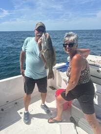 Two anglers proudly displaying a large Grouper caught during a sunny day on the water.