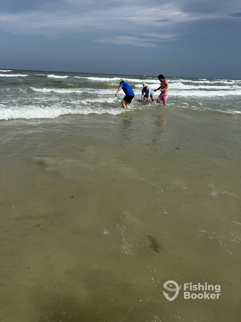 A group of individuals enjoying a day at the beach, wading in the shallow water, possibly engaging in fishing or crabbing activities.