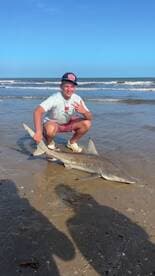 Young angler posing with a caught shark on the beach, showcasing a successful fishing trip.