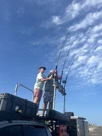 Two anglers on top of a vehicle, actively fishing with multiple rods against a clear blue sky.