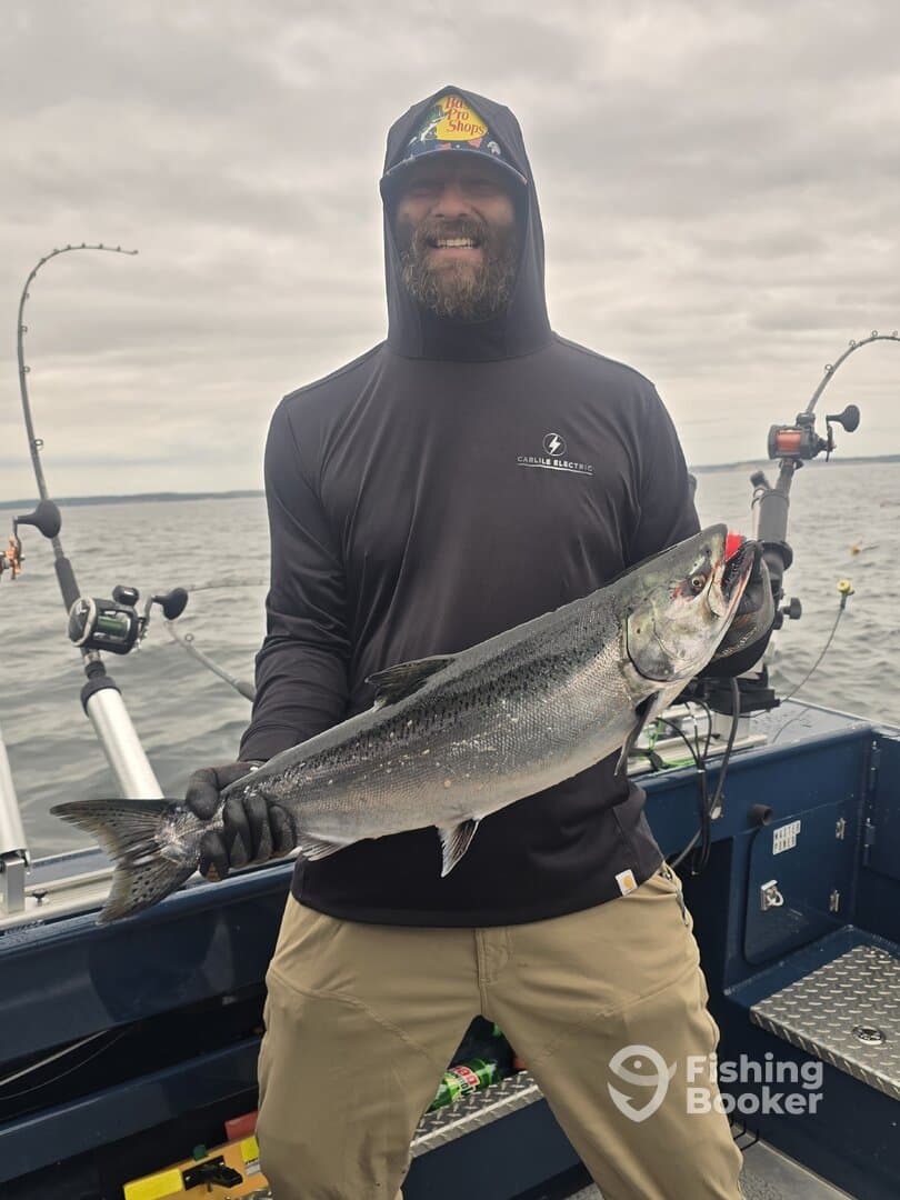A proud angler holding a large Salmon while fishing on a boat, showcasing a successful day on the water.
