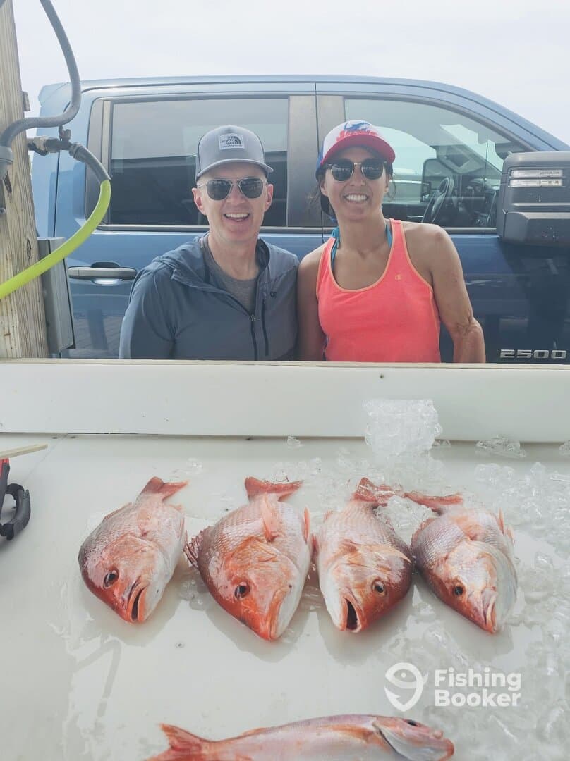 Two anglers smiling proudly next to a display of freshly caught Red Snapper on a fishing trip.