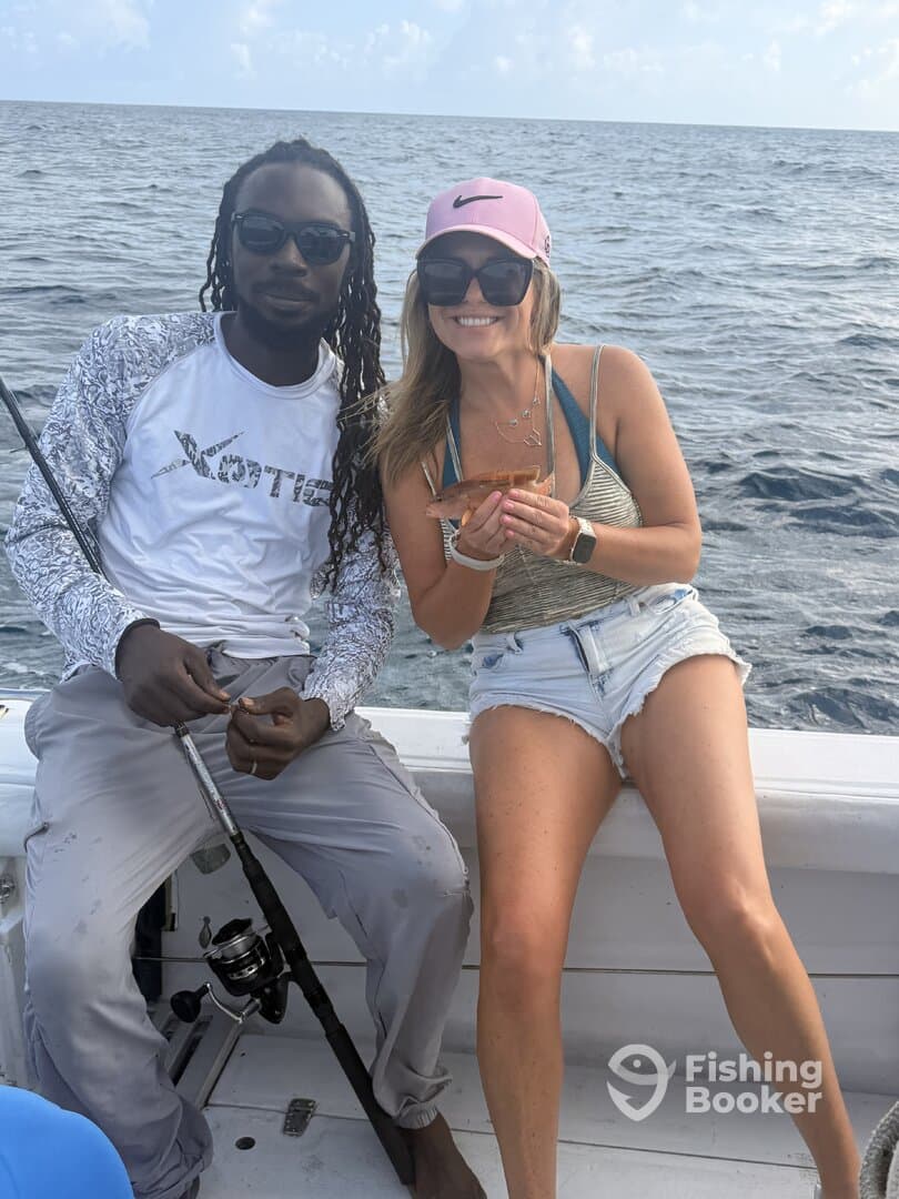 Two anglers enjoying a day on the water, with one proudly displaying a small fish while seated on the boat.