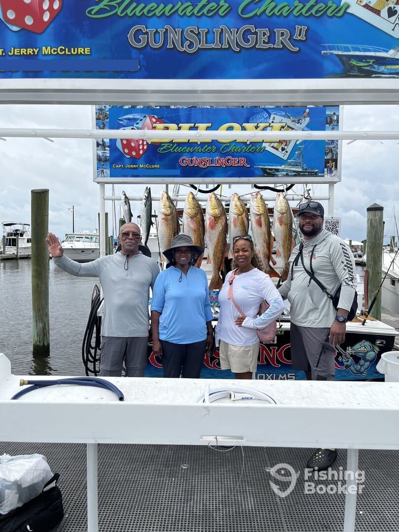A group of four anglers proudly posing in front of their catch of Redfish displayed on a board after a successful fishing trip with Bluewater Charters.