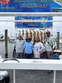 A group of four anglers proudly posing in front of their catch of Redfish displayed on a board after a successful fishing trip with Bluewater Charters.