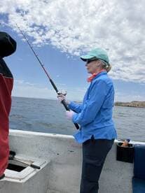 A woman actively fishing on a boat, casting her line into the water under a partly cloudy sky.