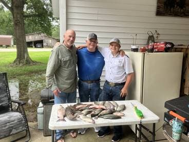 Three anglers proudly displaying their catch of various fish after a successful fishing trip, showcasing a family-friendly atmosphere.