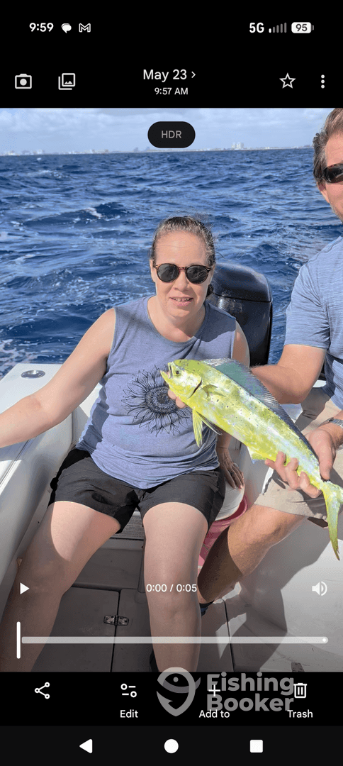 A woman proudly displays a vibrant Mahi Mahi while sitting on a boat, enjoying a sunny day on the water.