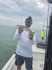 Angler proudly displaying a Speckled Trout while fishing on a boat in coastal waters.