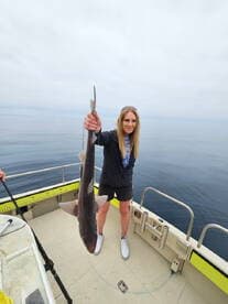 Angler proudly displaying a caught shark while fishing on a calm ocean, showcasing the excitement of deep-sea fishing.