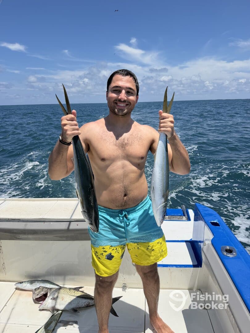 Angler proudly displaying two fish while aboard a boat in open waters, showcasing a successful fishing trip.