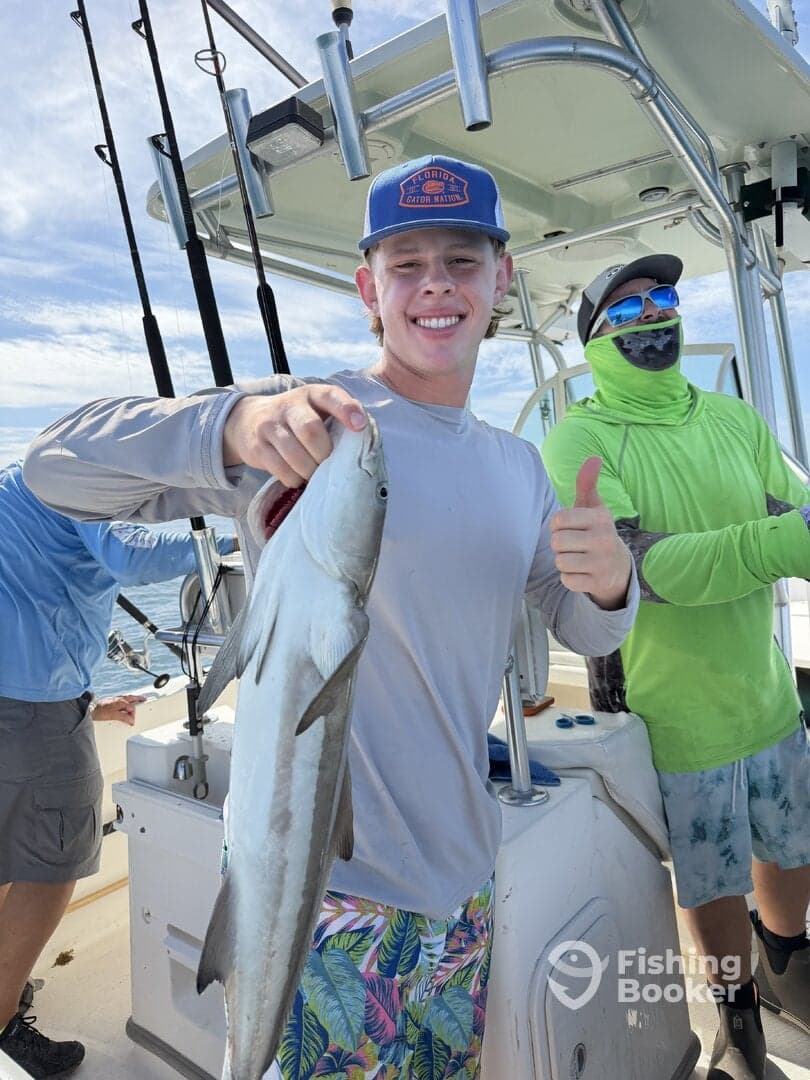A young angler proudly displaying a fish while fishing on a boat, surrounded by friends in a sunny coastal environment.