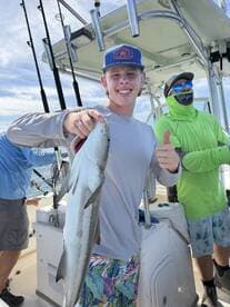 A young angler proudly displaying a fish while fishing on a boat, surrounded by friends in a sunny coastal environment.