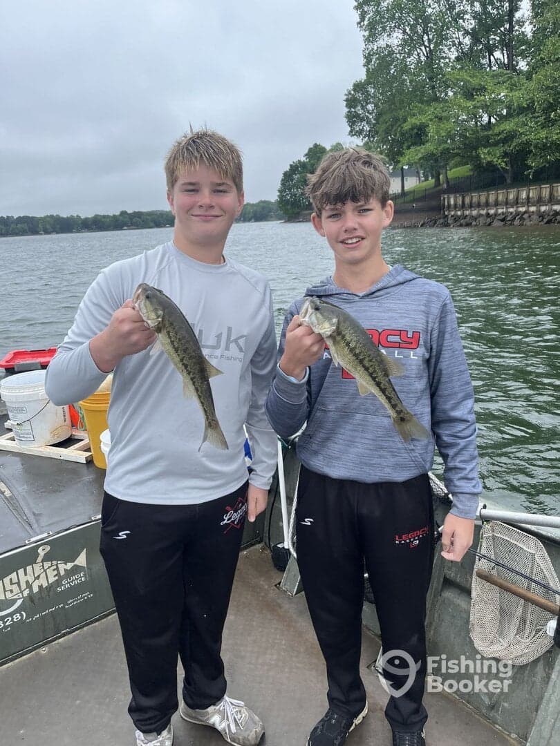 Two young anglers proudly displaying their catch of Largemouth Bass while fishing on a lake.