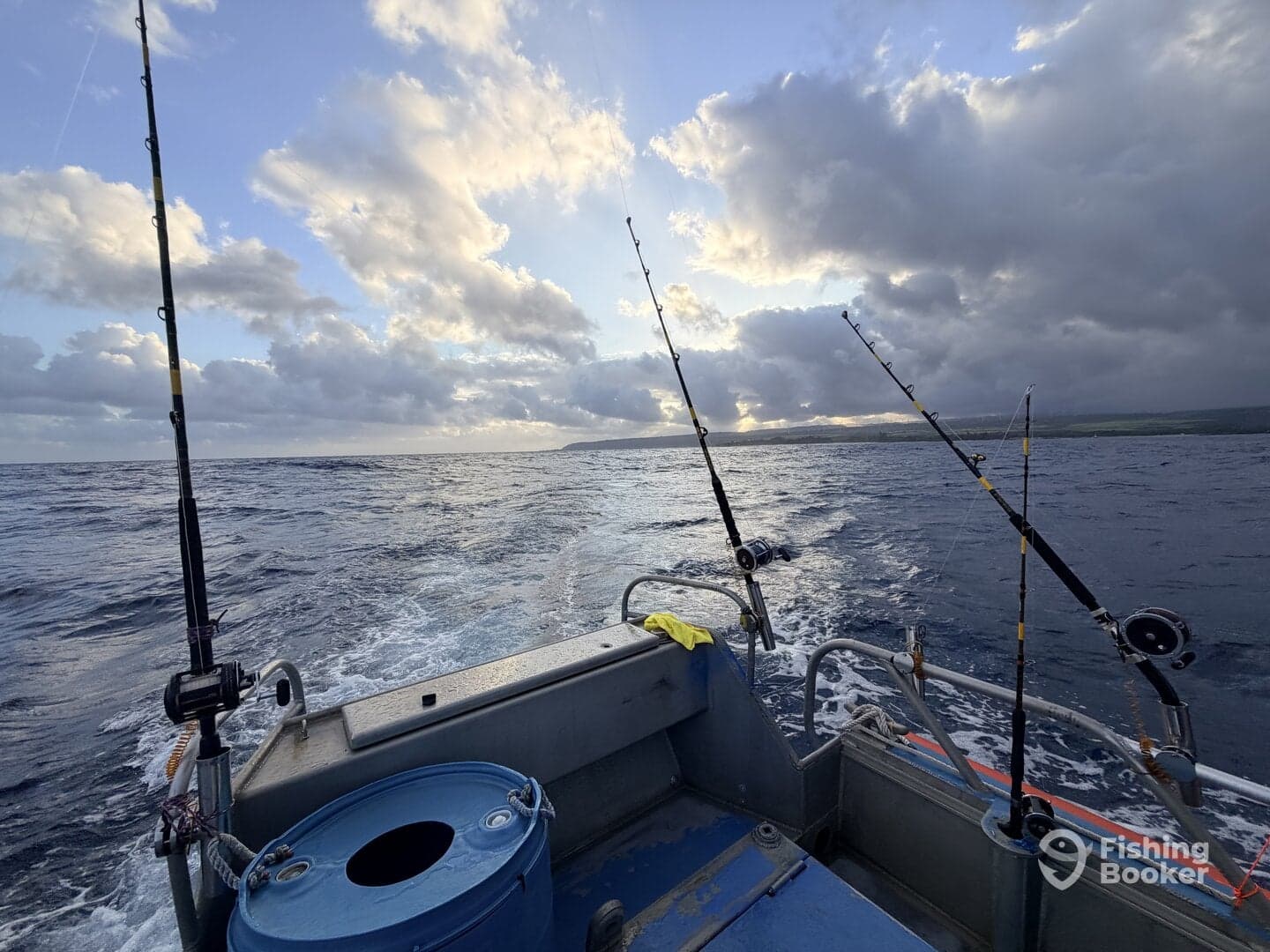 View from the helm of a fishing boat, showcasing fishing rods and a scenic ocean backdrop with clouds during a fishing trip.