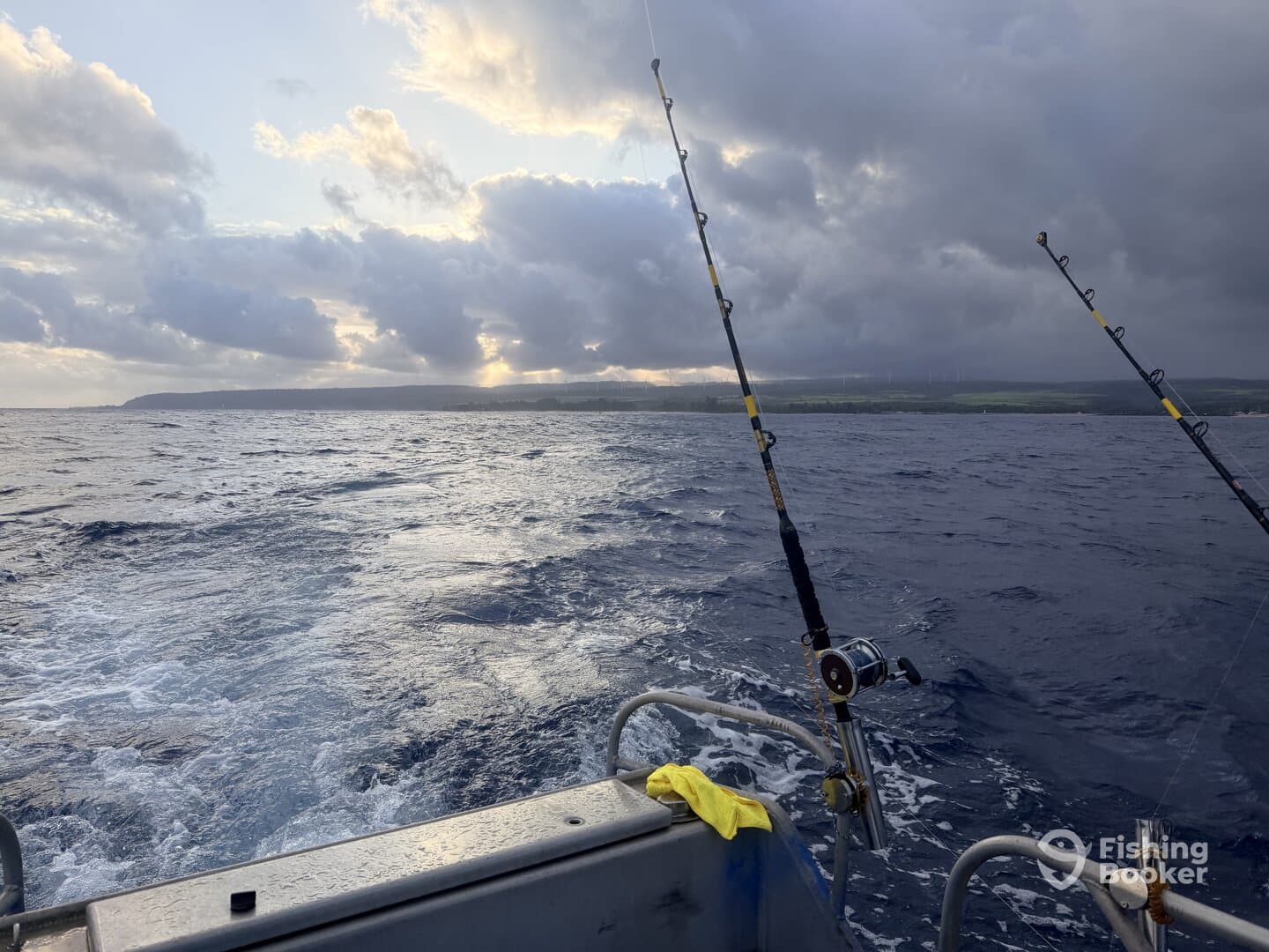 A scenic view from the side of a fishing boat, showcasing the open ocean and distant land under a dramatic sky.