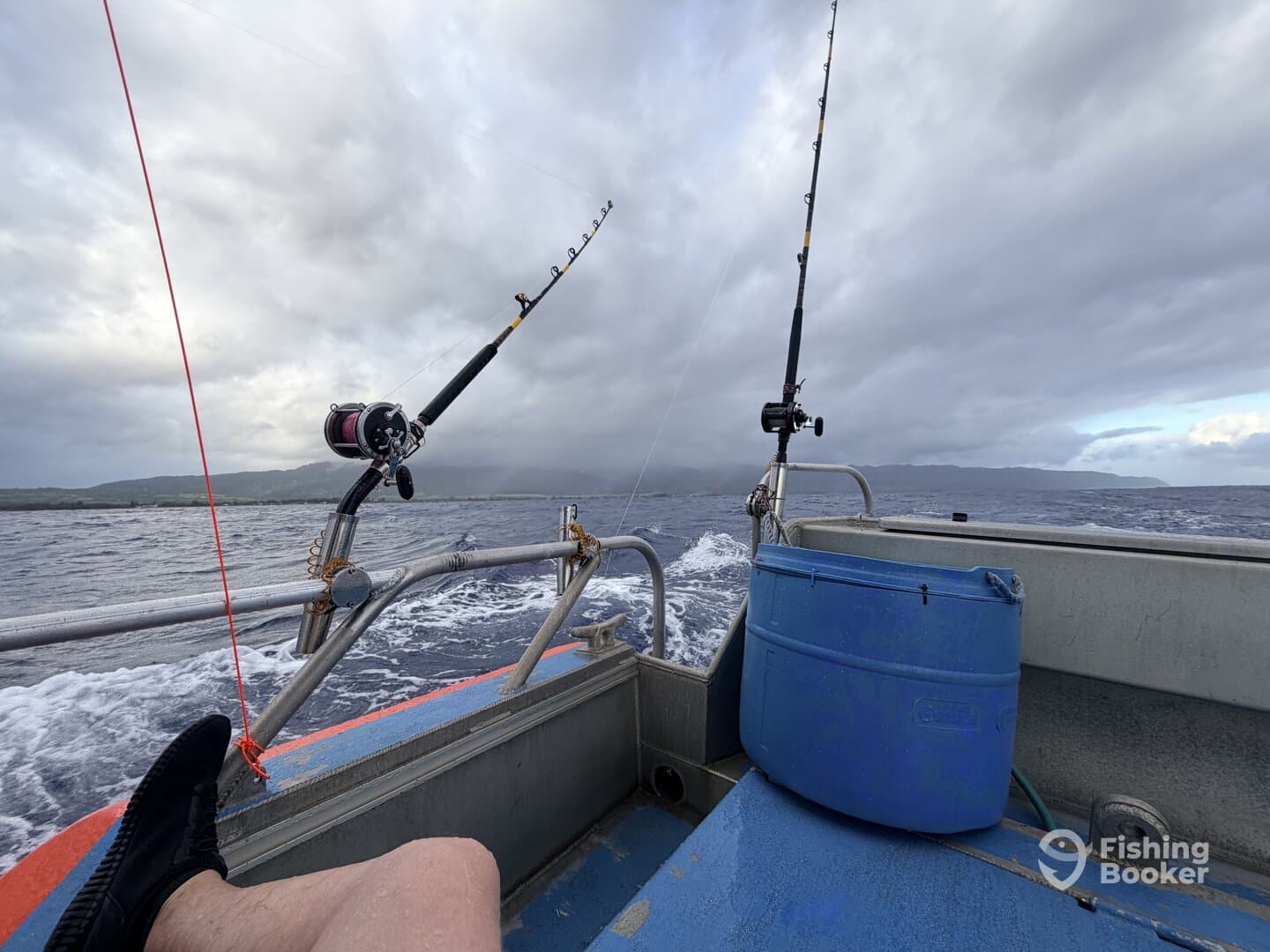 Interior view of a fishing boat showing fishing rods and a cooler, with a scenic backdrop of cloudy skies and distant land.