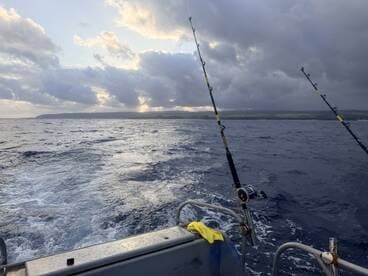 A scenic view from the side of a fishing boat, showcasing the open ocean and distant land under a dramatic sky.
