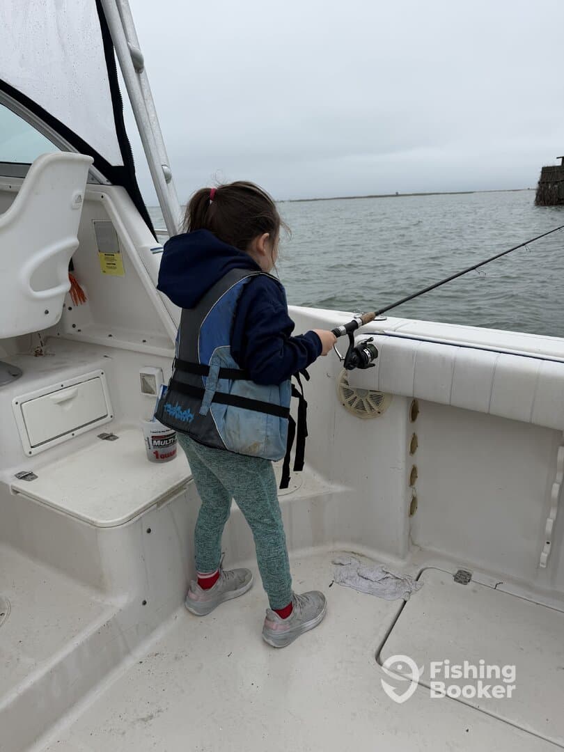 A young girl fishing from the deck of a boat, showcasing the excitement of angling in a calm water environment.