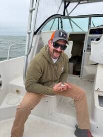 Angler holding a small fish while seated inside a boat, showcasing a casual fishing experience.