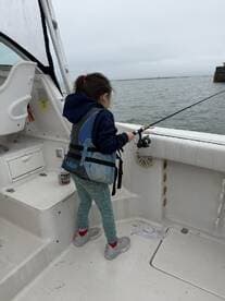 A young girl fishing from the deck of a boat, showcasing the excitement of angling in a calm water environment.