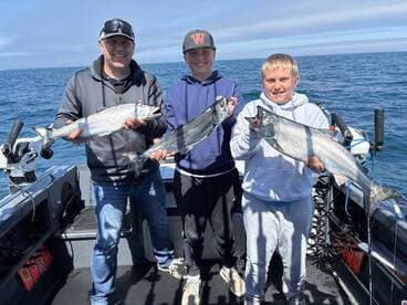 A family enjoying a successful fishing trip, proudly displaying their catch of salmon on a boat in open water.