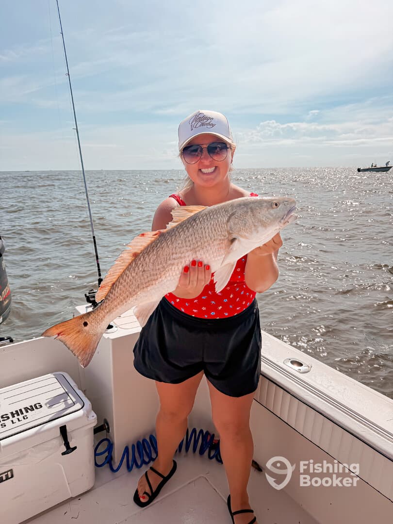 A happy angler proudly displaying a large Redfish while fishing on a sunny day.