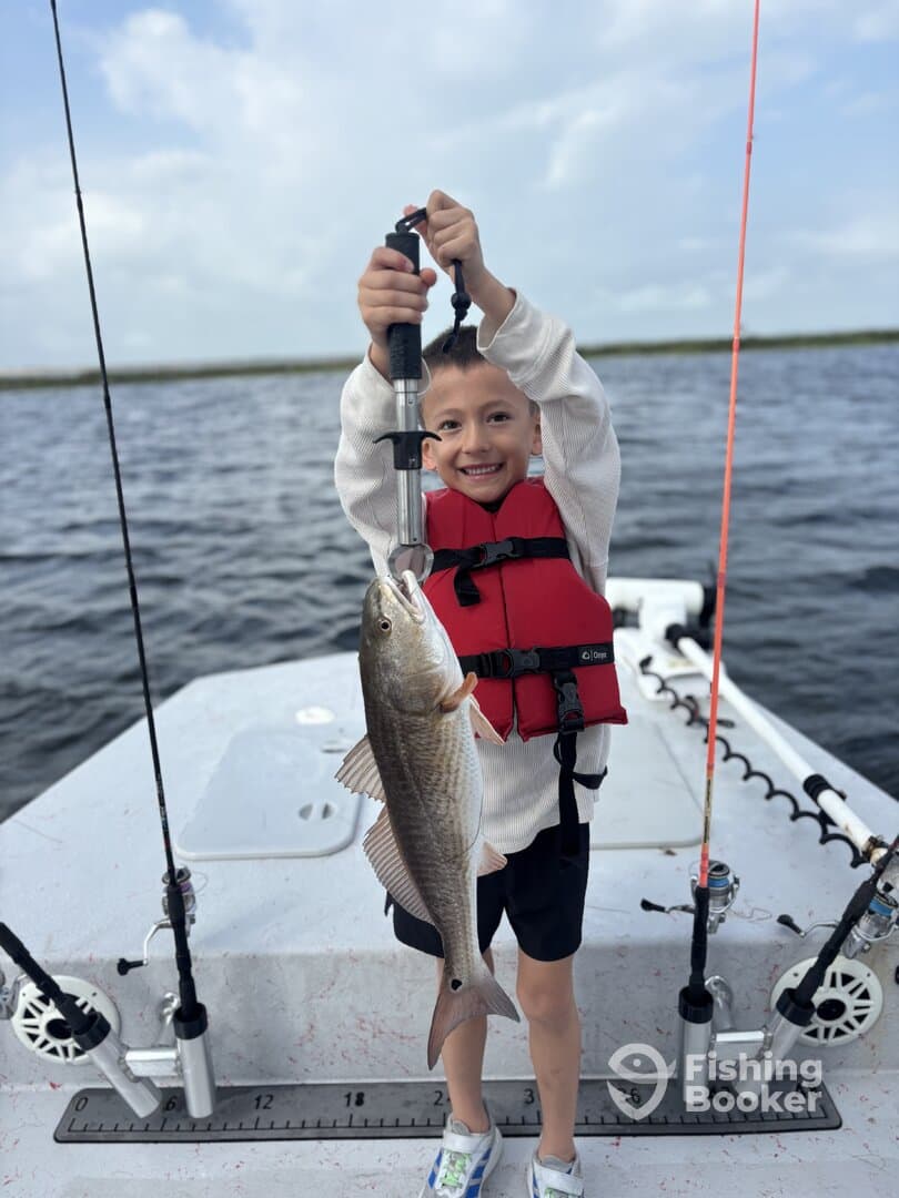 A young angler proudly holding a large Speckled Trout while fishing on a boat, showcasing a successful day on the water.