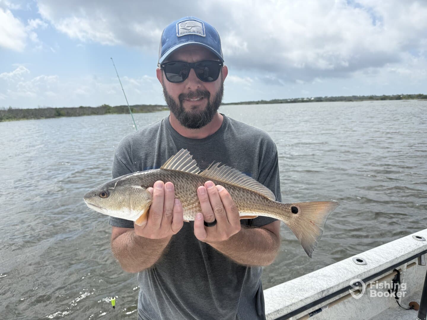 Angler proudly displaying a Redfish while fishing in a scenic coastal environment.